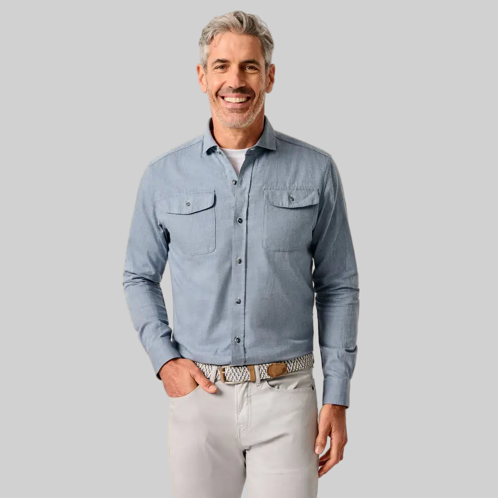 Man wearing a light blue button-up shirt and light gray pants against a beige background